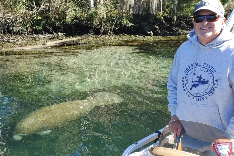 Captain Vince aboard the tour boat beside a manatee in clear water.