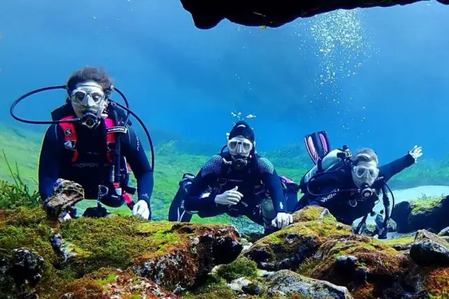 Three SCUBA divers swimming together over an underwater reef.