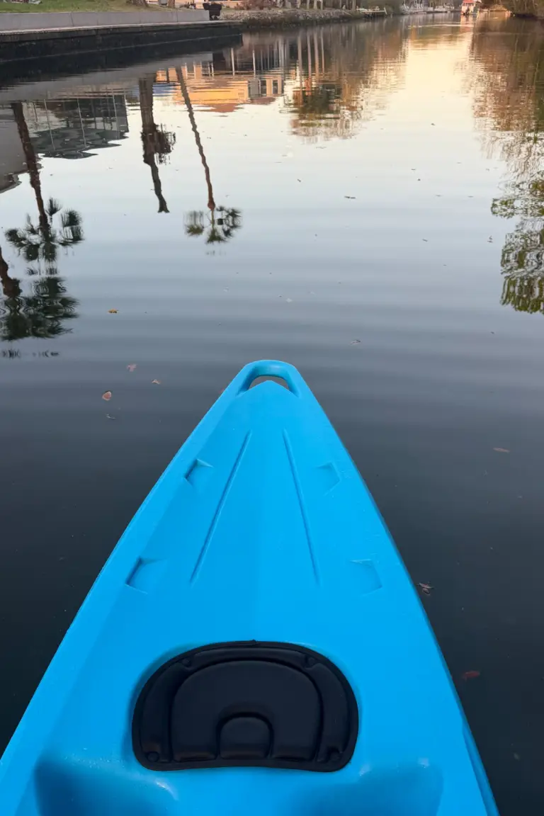 Bow of a blue kayak reflected in the calm canal.